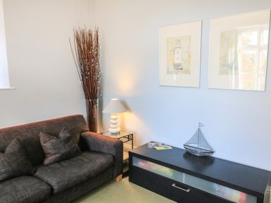 A sitting area with a dark sofa cushions a lamp on a glass side table a decorative boat and framed pictures on the wall at Victoria Lodge in Kingsbridge