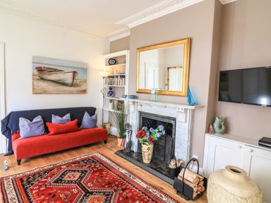 A living room with a red sofa pillows a fireplace with a gold framed mirror a red patterned rug and a wall mounted tv at Victoria Lodge in Kingsbridge