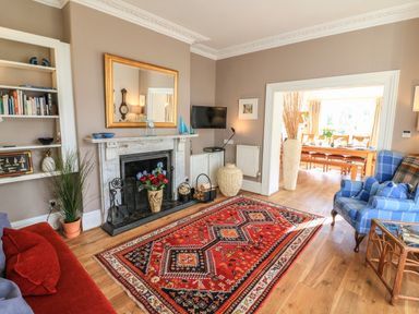 A living room with a fireplace a red patterned rug a blue armchair and a doorway to a dining area at Victoria Lodge in Kingsbridge