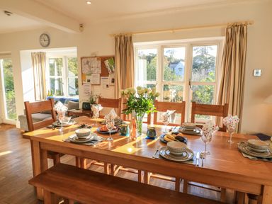 A dining table set with place settings and decorated with white roses in a room with windows and wooden furniture at Victoria Lodge in Kingsbridge