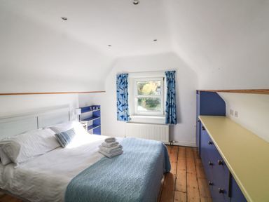 A bedroom with a bed with white linens and blue blanket blue cabinets and a window with blue curtains at Victoria Lodge in Kingsbridge