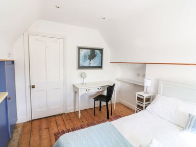 A bedroom with a white bed blue blanket a white desk with a chair and a framed picture on the wall at Victoria Lodge in Kingsbridge