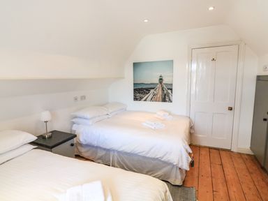 A bedroom with two beds a nightstand with a lamp a door and a painting of a lighthouse at Victoria Lodge in Kingsbridge