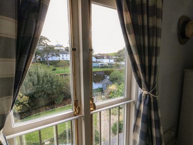 A window with blue and white plaid curtains looking out to trees and buildings at Victoria Lodge in Kingsbridge