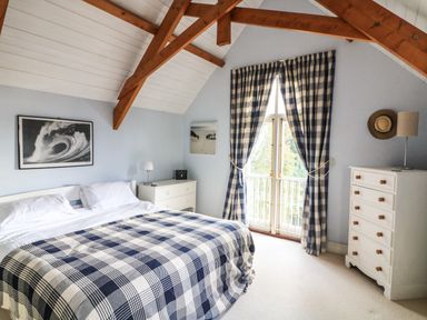 A bedroom with a double bed covered with a blue and white checked blanket two white dressers a window with blue and white checked curtains and wooden beams on the ceiling at Victoria Lodge in Kingsbridge