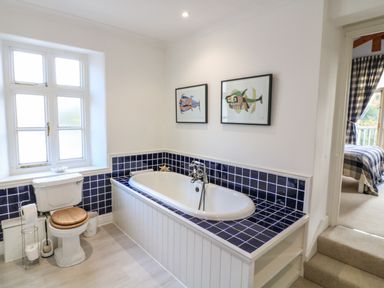 A bathroom with a bathtub surrounded by blue tiles a toilet and two framed fish artworks on the wall at Victoria Lodge in Kingsbridge