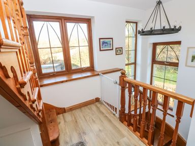 A staircase landing with wooden banisters and window frames and multiple windows showing an outdoor view at Nant Moel Isaf Farm in Rhydyfro near Pontardawe