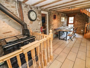 A dining area with a wooden table and benches beside a stone wall with a stove and clock at Nant Moel Isaf Farm in Rhydyfro near Pontardawe