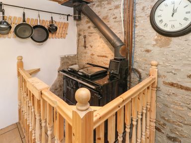 A corner with a black stove and hanging pans surrounded by wooden railing and stone walls at Nant Moel Isaf Farm Rhydyfro near Pontardawe