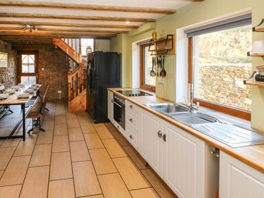 A kitchen with white cabinets a double sink and black refrigerator next to a dining table with benches at Nant Moel Isaf Farm in Rhydyfro near Pontardawe