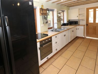 A kitchen with a black refrigerator an electric stove wooden countertops a double sink and white cabinets at Nant Moel Isaf Farm Rhydyfro near Pontardawe