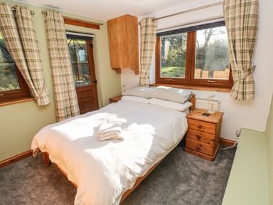 A bedroom with a double bed white bedding two bedside tables and wooden windows with plaid curtains at Nant Moel Isaf Farm in Rhydyfro near Pontardawe
