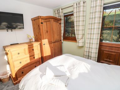 A bedroom with a wooden wardrobe and chest of drawers a mounted TV and a window with plaid curtains at Nant Moel Isaf Farm Rhydyfro near Pontardawe