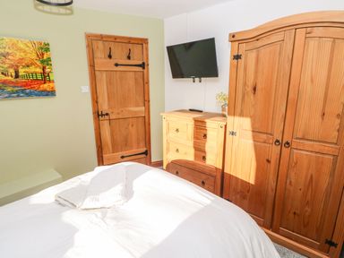 A bedroom with a bed towels wooden door wooden dresser wooden wardrobe and a wall mounted television at Nant Moel Isaf Farm in Rhydyfro near Pontardawe
