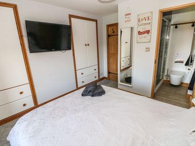 A bedroom with a bed and folded towels a wall mounted tv built in cupboards a mirror and an ensuite bathroom at Nant Moel Isaf Farm in Rhydyfro near Pontardawe