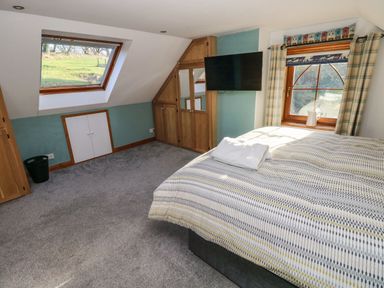 A bedroom with a bed, wall-mounted television, carpeted floor, wooden framed windows, and built-in wooden cupboards at Nant Moel Isaf Farm in Rhydyfro near Pontardawe