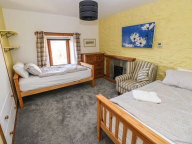 A bedroom with two wooden beds an armchair a chest of drawers and a fireplace at Nant Moel Isaf Farm Rhydyfro near Pontardawe