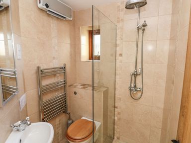A small bathroom with a shower, toilet with wooden seat, towel radiator, and a sink at Nant Moel Isaf Farm in Rhydyfro near Pontardawe