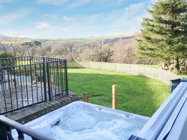 An outdoor hot tub with bubbling water overlooking a fenced grassy yard and trees at Nant Moel Isaf Farm in Rhydyfro near Pontardawe