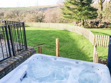 An outdoor hot tub with bubbling water overlooking a fenced green lawn and trees at Nant Moel Isaf Farm Rhydyfro near Pontardawe