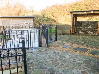 An outdoor area with a stone patio a fenced hot tub a covered seating area and a wooden shed at Nant Moel Isaf Farm in Rhydyfro near Pontardawe