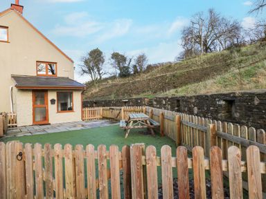 A fenced outdoor area with a picnic table next to a house and a stone retaining wall at Nant Moel Isaf Farm in Rhydyfro near Pontardawe