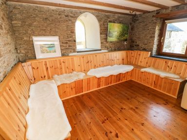 A corner seating area with wooden benches and white cushions in a room with stone walls and wooden floor at Nant Moel Isaf Farm in Rhydyfro near Pontardawe