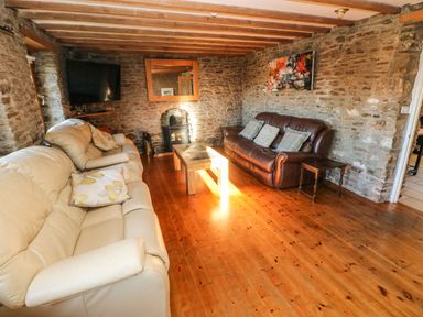 A living room with leather sofas wooden coffee table and stone walls at Nant Moel Isaf Farm in Rhydyfro near Pontardawe