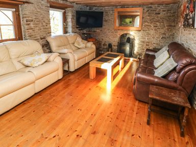 A living room with three sofas a wooden coffee table a wall-mounted tv and a fireplace at Nant Moel Isaf Farm in Rhydyfro near Pontardawe