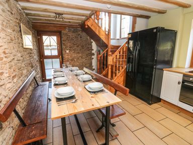 A dining area with a wooden table set with plates and glasses next to a stone wall and wooden stairs at Nant Moel Isaf Farm in Rhydyfro near Pontardawe