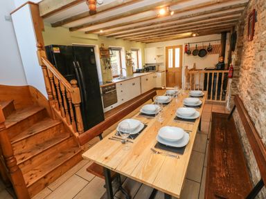 A kitchen and dining area with a wooden table set for eight and wooden stairs at Nant Moel Isaf Farm Rhydyfro near Pontardawe