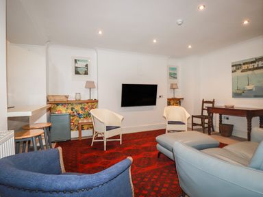 A living room with chairs a wall mounted television a red rug and a wooden table at Melvill Lower Deck in Falmouth