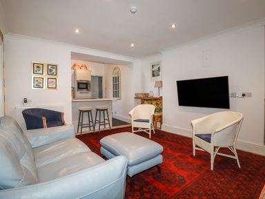 A living room with a sofa ottoman armchairs and wall mounted television at Melvill Lower Deck in Falmouth
