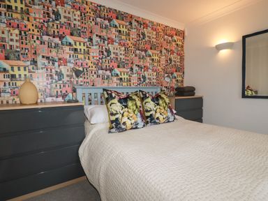 A bedroom with a bed between two dressers and a colorful house pattern wallpaper at Melvill Lower Deck in Falmouth