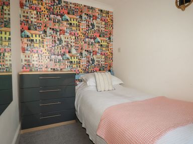 A bedroom with a single bed a chest of drawers and a wall with colorful building wallpaper at Melvill Lower Deck in Falmouth