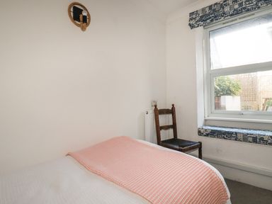 A bedroom with a bed covered in white and pink linens a wooden chair and a window with patterned cushions at Melvill Lower Deck in Falmouth