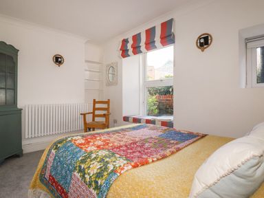 A bedroom with a bed covered in a floral patchwork quilt a wooden chair a green cabinet and a window with a striped blind at Melvill Lower Deck in Falmouth