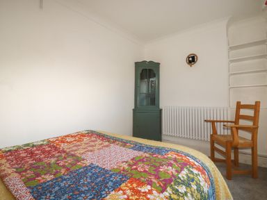 A bedroom with a patchwork quilt on the bed a wooden chair a green corner cabinet and a white radiator at Melvill Lower Deck in Falmouth