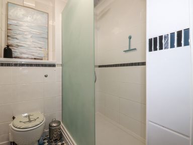 A bathroom with a toilet a framed painting a small trash can and a shower with a frosted glass door at Melvill Lower Deck in Falmouth
