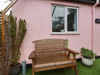 A wooden bench outside a pink building with a window and plants in pots at Melvill Lower Deck in Falmouth