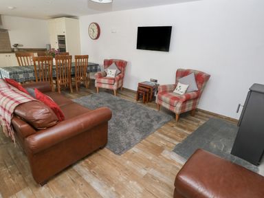 A living room with brown leather sofa and two plaid armchairs a dining table with wooden chairs and a wall mounted TV at Y Beudy Crosswell Eglwyswrw near Newport Pembrokeshire