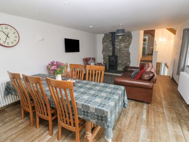 A dining area with wooden chairs around a table and a living space with a brown sofa near a stone fireplace at Y Beudy in Crosswell Eglwyswrw near Newport Pembrokeshire