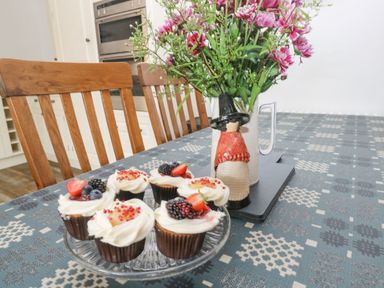 A dining table with a plate of decorated cupcakes and a vase of pink flowers with a figurine at Y Beudy in Crosswell Eglwyswrw near Newport Pembrokeshire