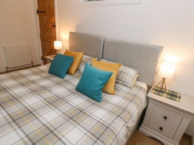 A bedroom with a double bed with checkered bedspread and blue and yellow pillows at Y Beudy Crosswell Eglwyswrw near Newport Pembrokeshire