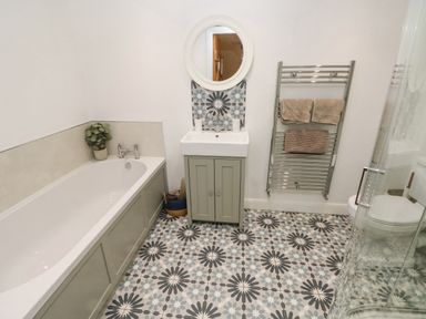 A bathroom with a bathtub a sink with a round mirror a heated towel rack and a shower at Y Beudy in Crosswell Eglwyswrw near Newport Pembrokeshire