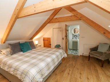 A bedroom with wooden beams a bed an armchair and a door leading to a bathroom at Y Beudy in Crosswell Eglwyswrw near Newport Pembrokeshire