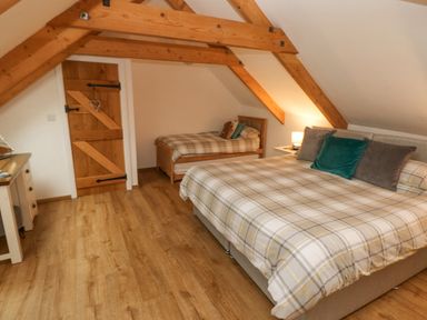 A bedroom with a large bed and a single bed under wooden beams at Y Beudy in Crosswell Eglwyswrw near Newport Pembrokeshire