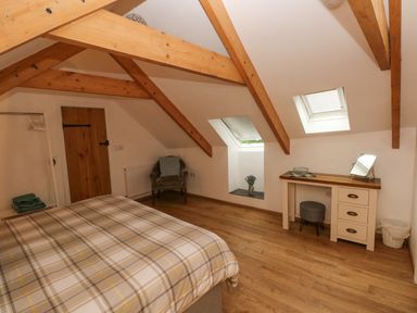 A bedroom with a bed a wooden desk with a mirror a gray chair and wooden beams on the ceiling at Y Beudy in Crosswell Eglwyswrw near Newport Pembrokeshire
