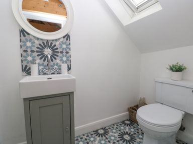 A bathroom with a sink and cabinet a round mirror a toilet a plant on the toilet and patterned floor tiles at Y Beudy in Crosswell Eglwyswrw near Newport Pembrokeshire