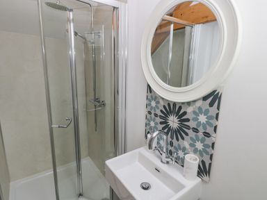 A bathroom with a glass shower enclosure a white sink a round mirror and patterned tiles at Y Beudy Crosswell Eglwyswrw near Newport Pembrokeshire